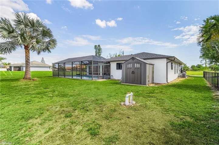 Back of house with a storage unit, a lawn, and a lanai