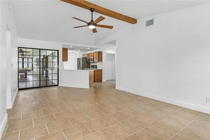 Unfurnished living room featuring ceiling fan, vaulted ceiling with beams, and light tile floors