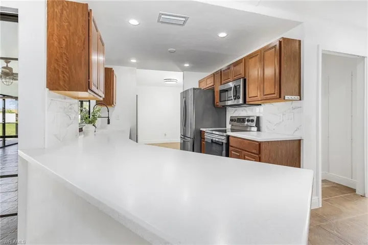Kitchen with kitchen peninsula, stainless steel appliances, tasteful backsplash, sink, and light tile floors