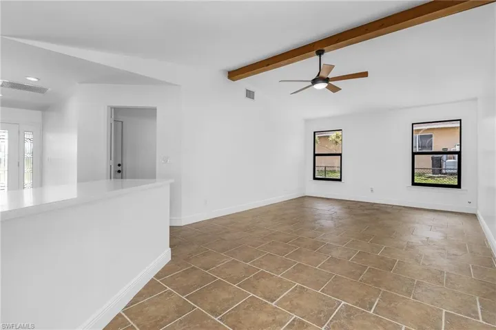 Unfurnished living room featuring ceiling fan, tile flooring, and lofted ceiling with beams