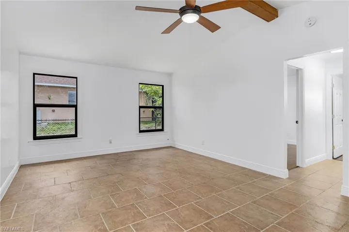 Unfurnished room featuring a wealth of natural light, lofted ceiling with beams, light tile flooring, and ceiling fan
