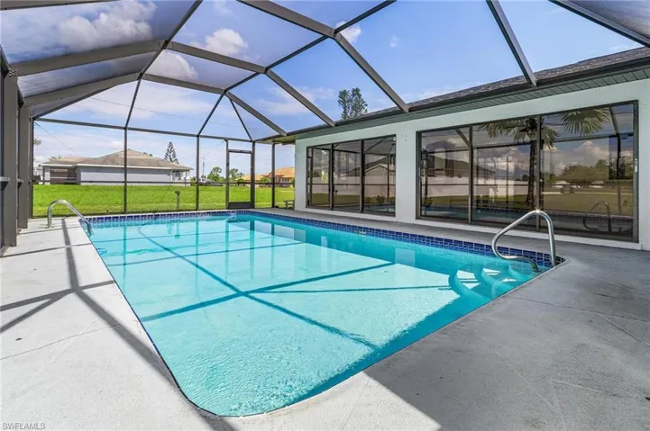 View of pool with a lawn, glass enclosure, and a patio area