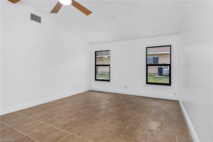 Spare room featuring a healthy amount of sunlight, lofted ceiling, ceiling fan, and tile floors