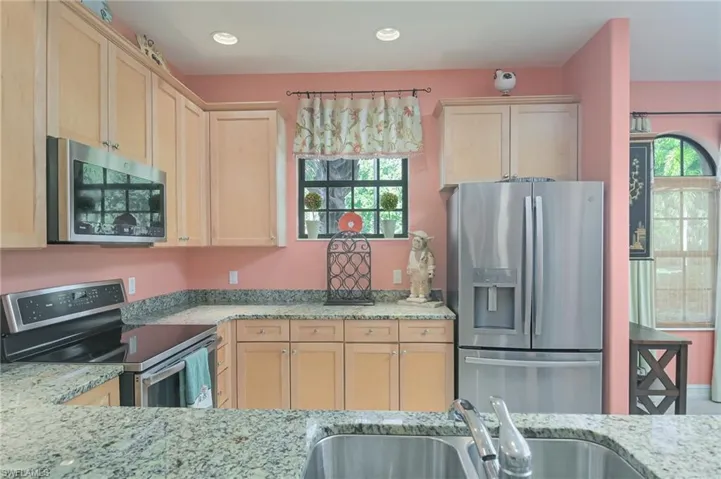 Kitchen with appliances with stainless steel finishes, sink, light stone countertops, and light brown cabinets