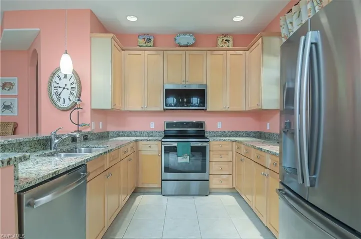 Kitchen with light tile flooring, stainless steel appliances, hanging light fixtures, light stone countertops, and sink