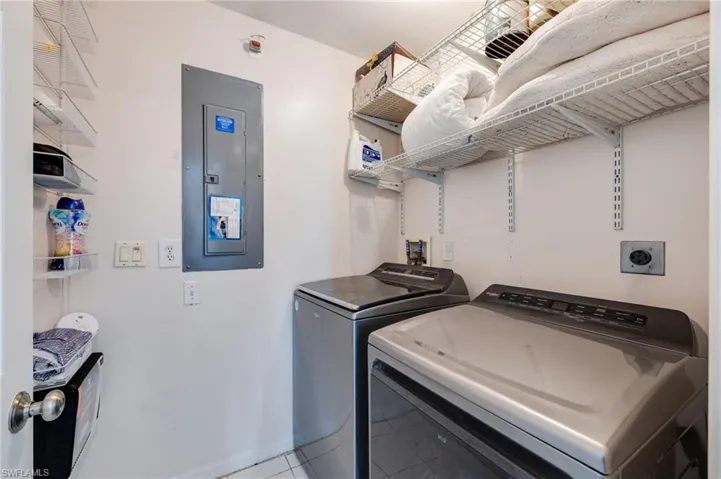 Laundry room with electric panel, tile patterned flooring, and washer and clothes dryer