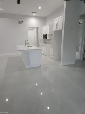 Kitchen with sink, light tile patterned flooring, white cabinetry, and a center island with sink
