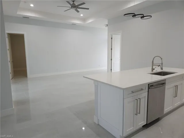 Kitchen with a center island with sink, dishwasher, ceiling fan, a tray ceiling, and sink