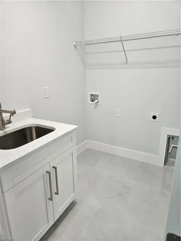Laundry area with light tile patterned flooring, sink, electric dryer hookup, cabinets, and hookup for a washing machine