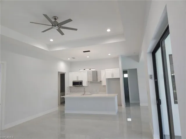 Kitchen with tasteful backsplash, white cabinets, ceiling fan, a raised ceiling, and a center island with sink
