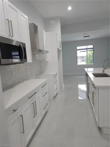 Kitchen with light tile patterned flooring, extractor fan, sink, and white cabinets