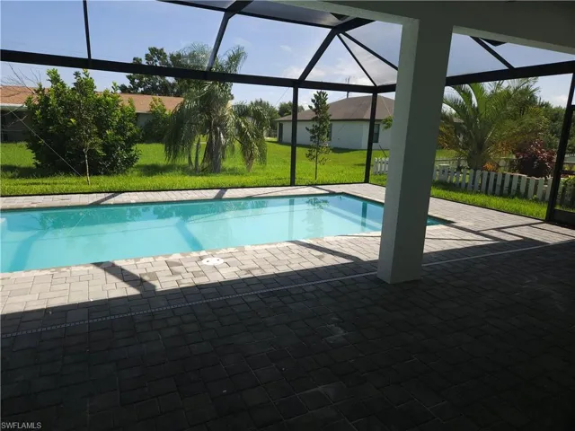 View of swimming pool with glass enclosure, a patio area, and a yard
