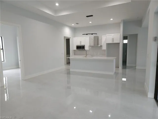 Kitchen with decorative light fixtures, white cabinetry, tasteful backsplash, wall chimney range hood, and a kitchen island with sink