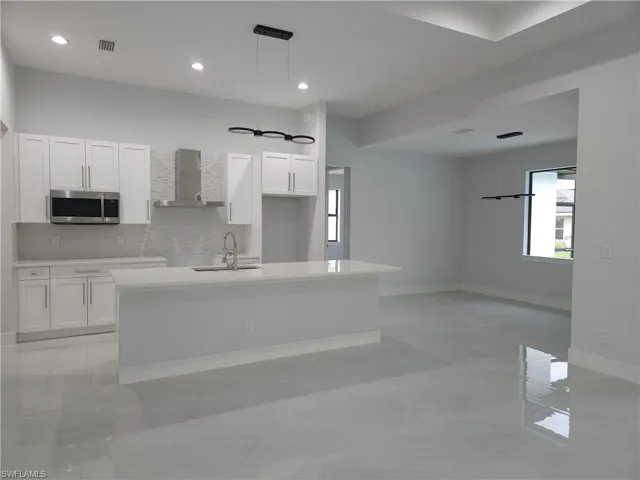 Kitchen with white cabinetry, light tile patterned floors, wall chimney range hood, an island with sink, and sink
