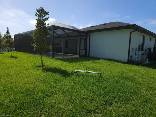 Rear view of property with glass enclosure and a lawn