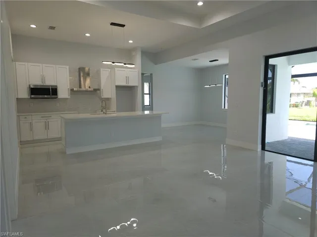 Kitchen featuring light tile patterned flooring, white cabinetry, pendant lighting, and wall chimney range hood