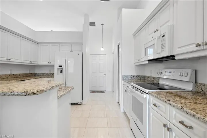 Kitchen featuring white appliances, white cabinets, light stone countertops, pendant lighting, and light tile patterned floors
