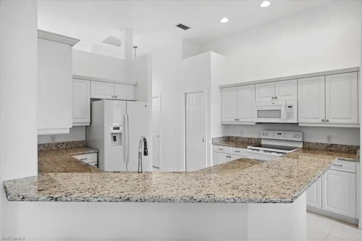 Kitchen with white appliances, light stone countertops, white cabinetry, a towering ceiling, and recessed lighting