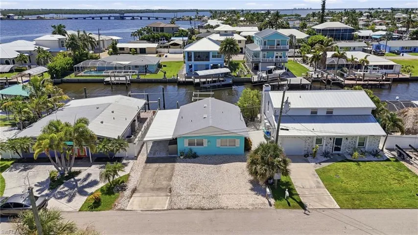 Waterfront home featuring a turquoise exterior with metal roof, mature palm landscaping, and direct canal access