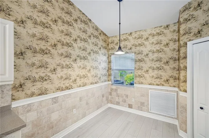 Unfurnished dining area featuring a wainscoted wall, wallpapered walls, and wood finished floors