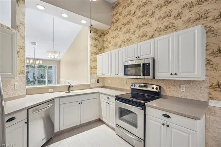 Kitchen featuring wallpapered walls, stainless steel appliances, a chandelier, white cabinetry, and light countertops