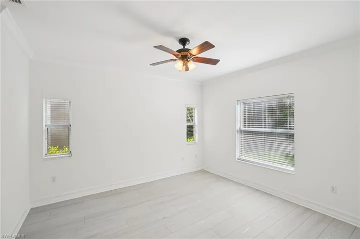 Spare room with plenty of natural light, ornamental molding, ceiling fan, and light wood-style flooring