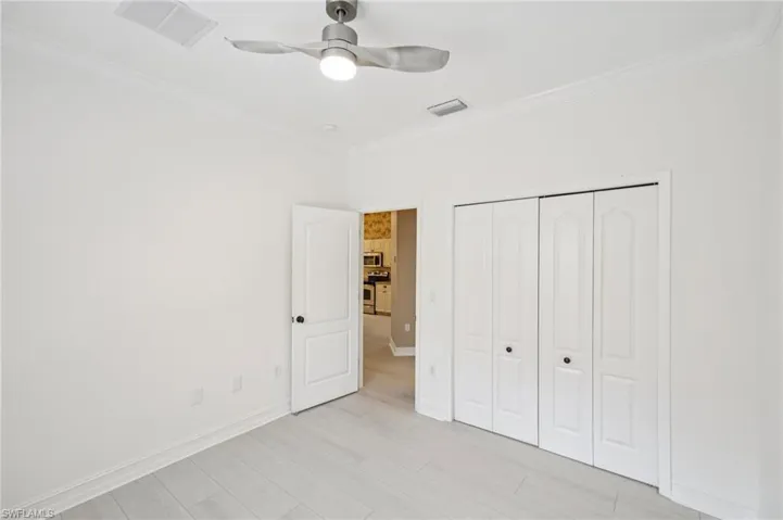 Unfurnished bedroom with crown molding, a closet, light wood-type flooring, and a ceiling fan