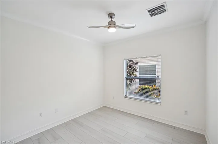 Empty room with ornamental molding, ceiling fan, and light wood-style floors