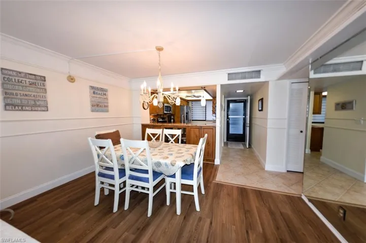 VIEW FROM DINING AREA TOWARDS KITCHEN AND UNIT ENTRANCE.  ENTRANCE TO GUEST BEDROOM, GUEST BATH AND LAUNDRY ROOM IS TO MIDDLE RIGHT.  LUXURY VINYL TILE WOOD LOOK PLANK FLOORING.  CROWN MOLDING.