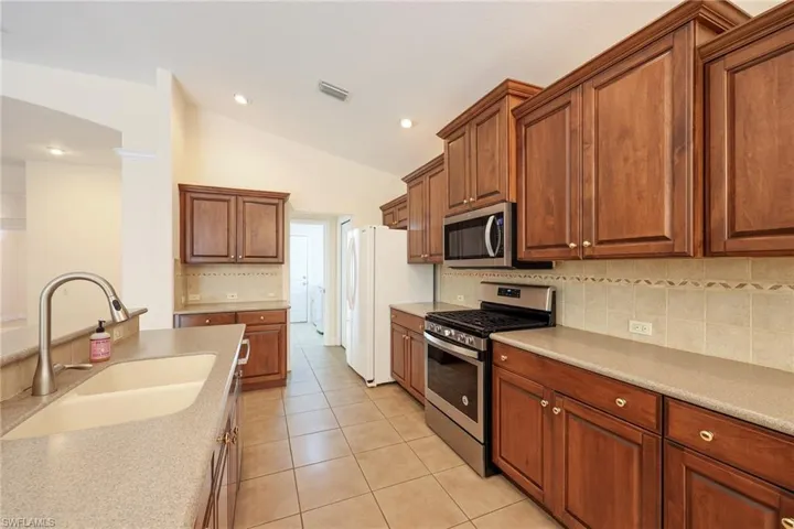 Kitchen with lofted ceiling, sink, light tile patterned floors, appliances with stainless steel finishes, and tasteful backsplash