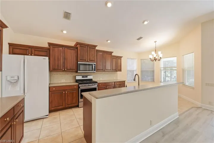 Kitchen with backsplash, hanging light fixtures, stainless steel appliances, a notable chandelier, and a center island with sink