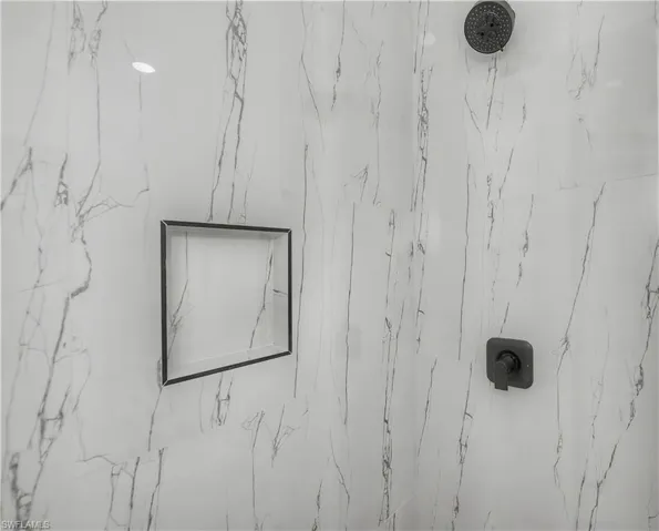 Shower enclosure with marble-look tile, a matte black rain shower head, a built-in shower niche, and a matte black shower control