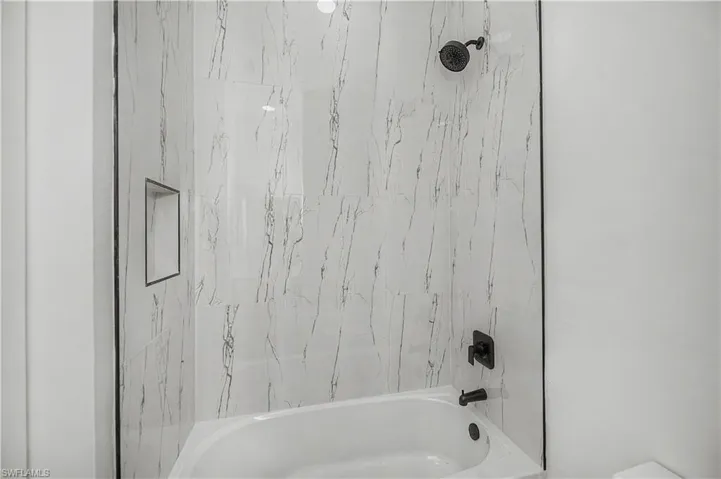 Built-in bathtub with black fixtures, large-format tile surround, and an integrated shower niche