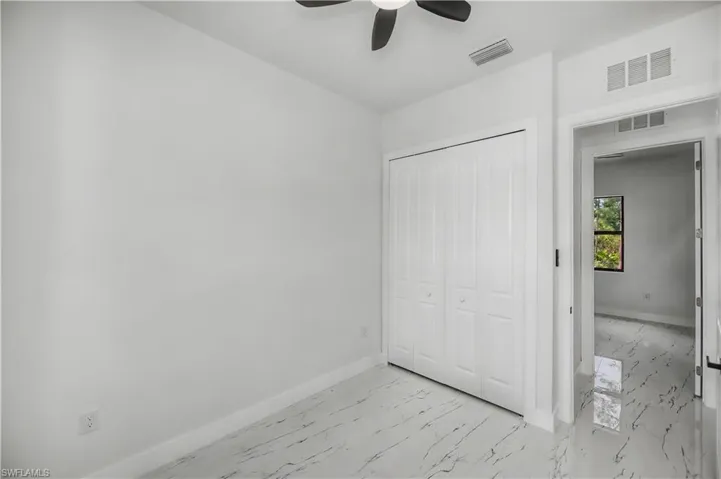 White bi-fold closet doors, ceiling fan, white walls, and marble-look flooring