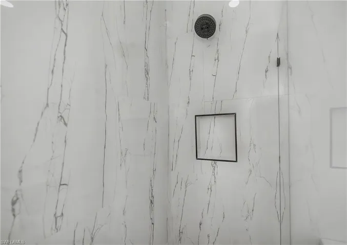 Shower with marble-look tile, dark-finish shower head, and recessed wall niche with dark trim