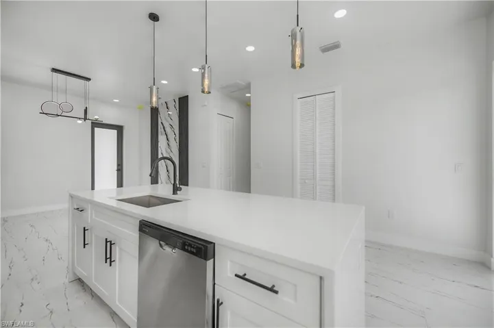 Kitchen island with a white countertop and integrated sink, stainless steel dishwasher, pendant lighting, and white cabinetry with black hardware
