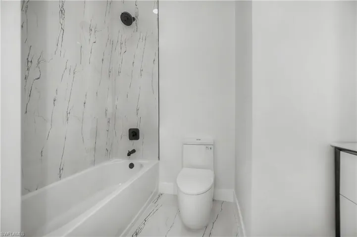 Bathtub with a shower, marble-look wall tiling, and a black-finish shower system