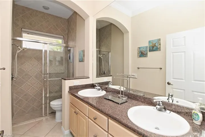Full bathroom featuring a shower stall, double vanity, light tile patterned floors, and ornamental molding