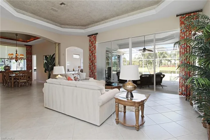 Tiled living area with a tray ceiling, arched walkways, plenty of natural light, a chandelier, and a textured ceiling