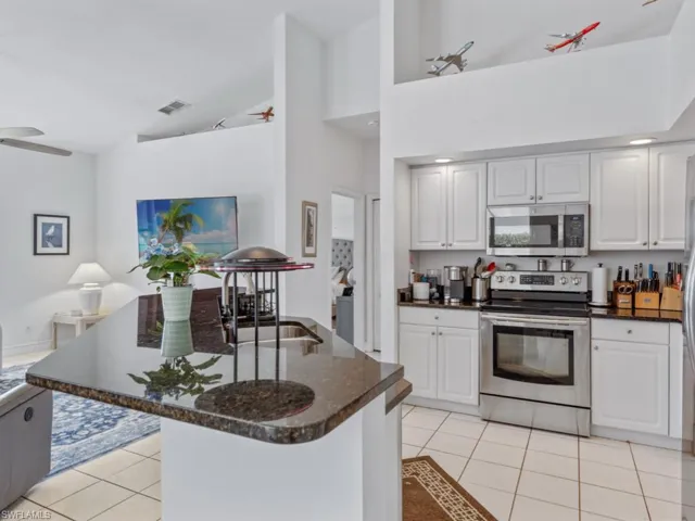 Kitchen featuring light tile patterned flooring, white cabinetry, appliances with stainless steel finishes, visible vents, and dark stone counters