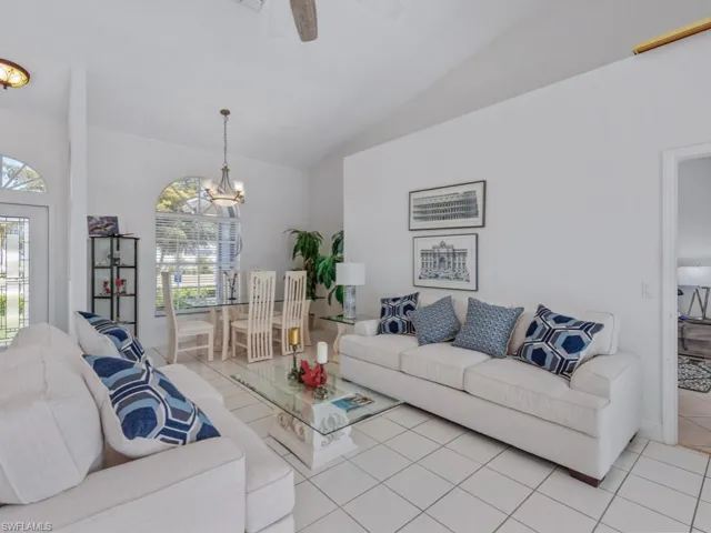 Living room featuring vaulted ceiling, light tile patterned floors, and ceiling fan with notable chandelier