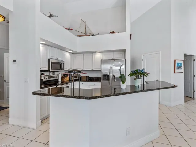 Kitchen featuring dark stone counters, a high ceiling, appliances with stainless steel finishes, and light tile patterned floors