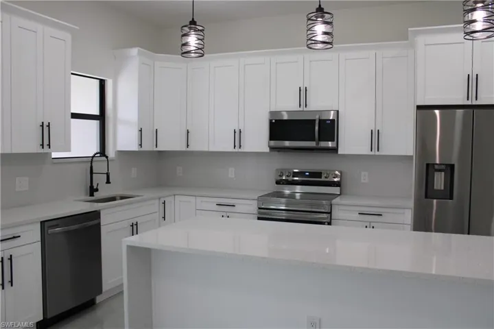 Modern kitchen featuring white shaker cabinetry with matte black hardware, stainless steel appliances, quartz countertops, and a full-height tile backsplash
