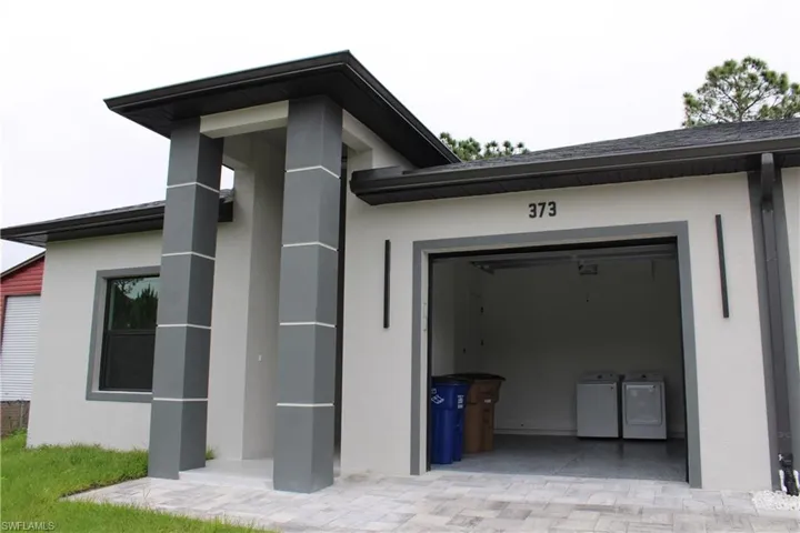 Contemporary exterior with a covered entry featuring architectural columns, a window with dark trim, an attached garage with an epoxy-coated floor, and a paver driveway