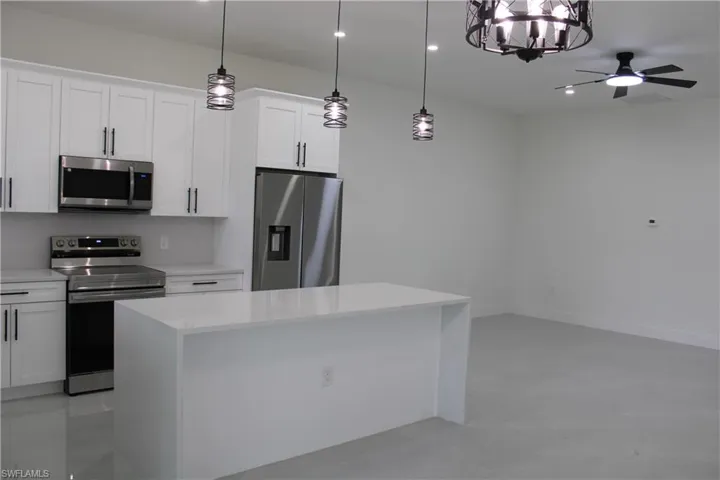 Modern kitchen featuring white shaker cabinetry, stainless steel appliances, a center island with a light-colored countertop, and contemporary pendant lighting