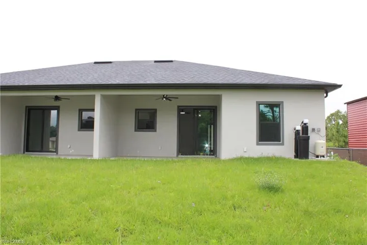 Rear exterior featuring a covered patio with two ceiling fans, multiple windows with dark frames, and sliding glass doors