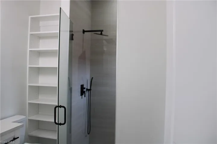 Walk-in shower with clear glass enclosure and matte black fixtures, complemented by a built-in white shelving unit