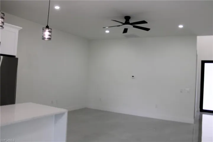 Open-concept room featuring a modern black ceiling fan, recessed lighting, and a white kitchen island with a light-toned countertop