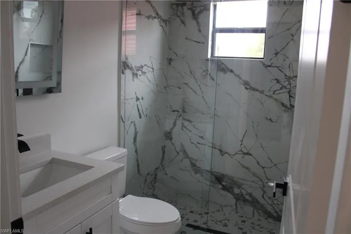 Modern bathroom featuring a walk-in shower with floor-to-ceiling marbled tile, a glass shower enclosure, and a built-in shower niche