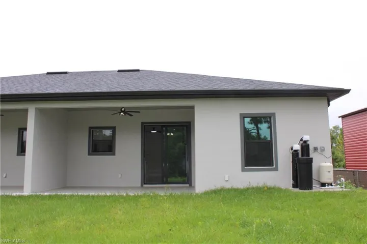 Rear exterior featuring a covered patio with a ceiling fan, sliding glass doors, and dark-framed windows
